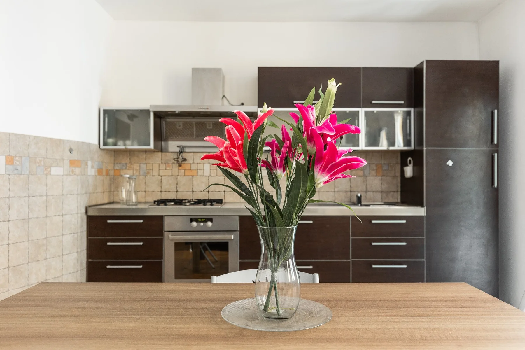 A kitchen with dark cabinets and a vase of bright flowers on the table.