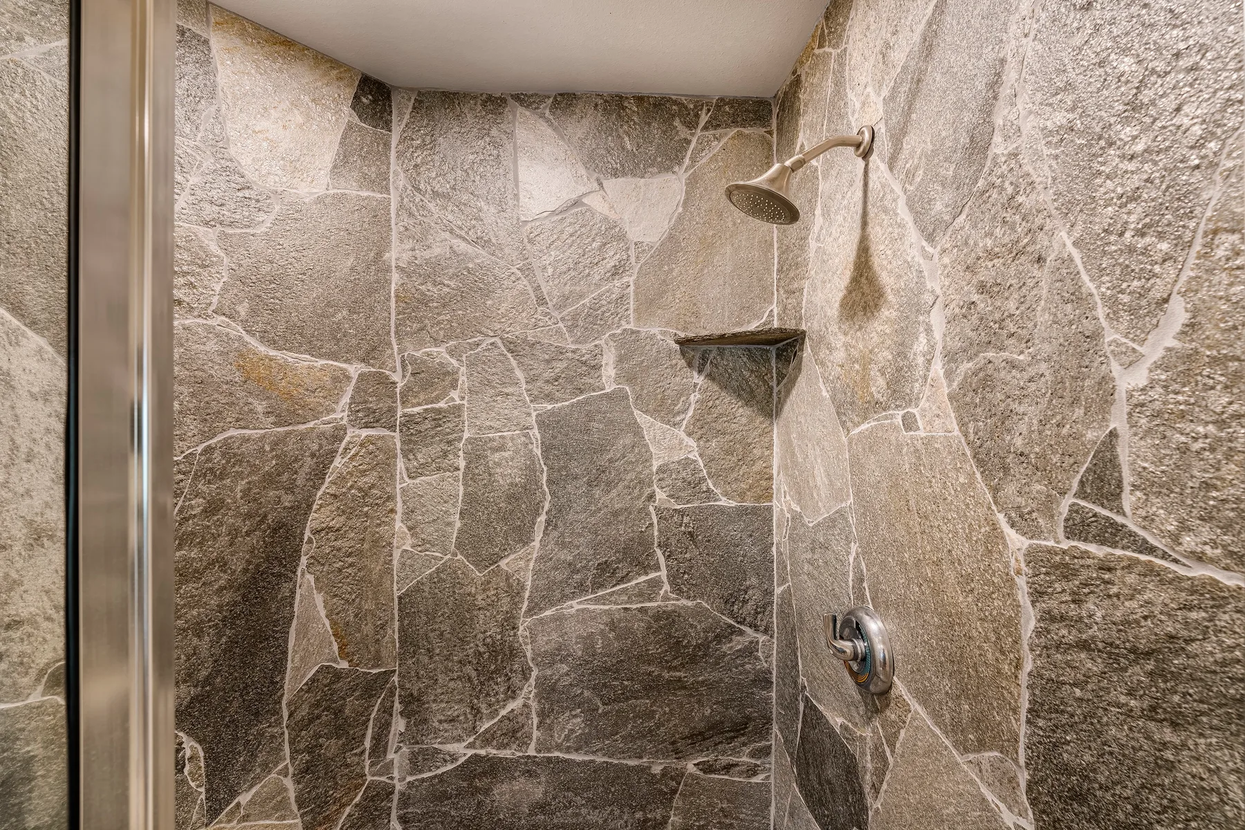 Una ducha con azulejos, cabezal de ducha y controles en la pared.