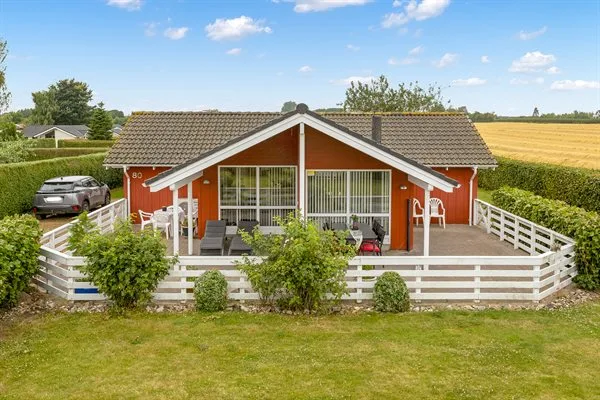 A red house with a fenced patio, outdoor seating, and open fields beyond.