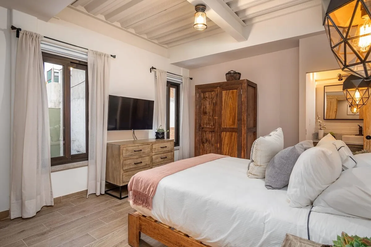 A bedroom with a neatly made bed, wooden dresser, and television.