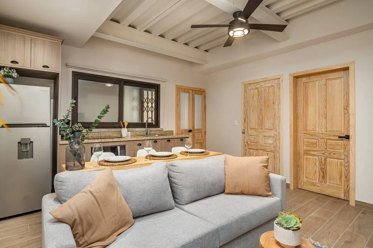 Una sala de estar con un sofá gris, una mesa de comedor y una cocina al fondo.