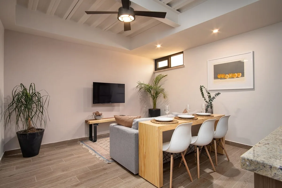 Un comedor con una mesa de madera y asientos blancos bajo un ventilador de techo.