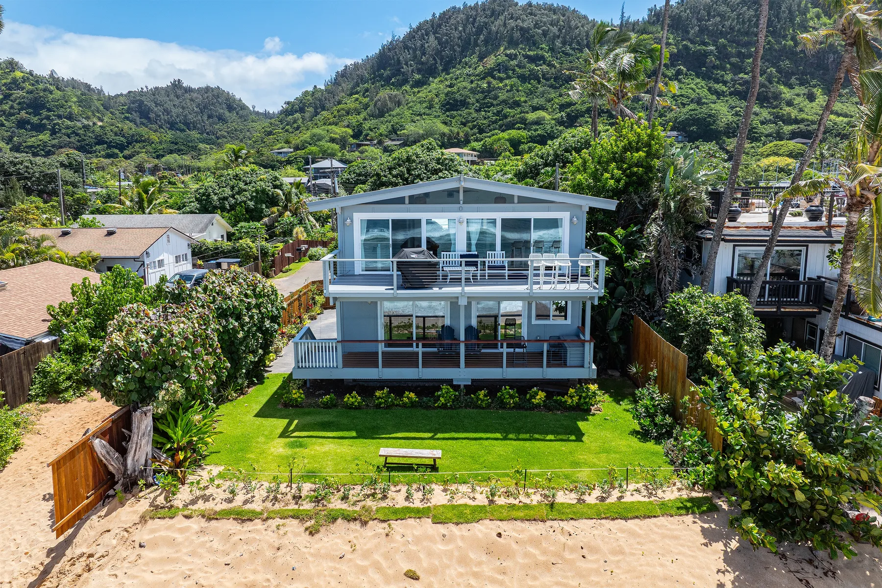 A modern house stands beside a sandy beach, surrounded by green hills.
