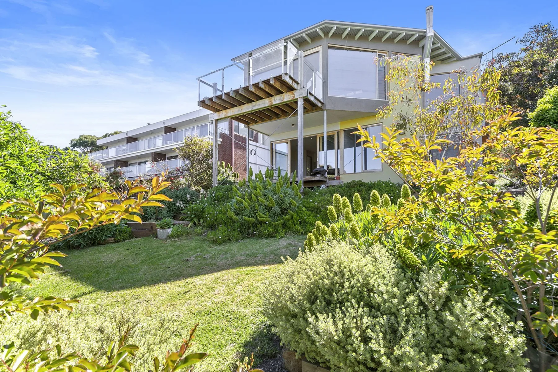 Una casa moderna da a un jardín ajardinado con arbustos verdes y árboles.