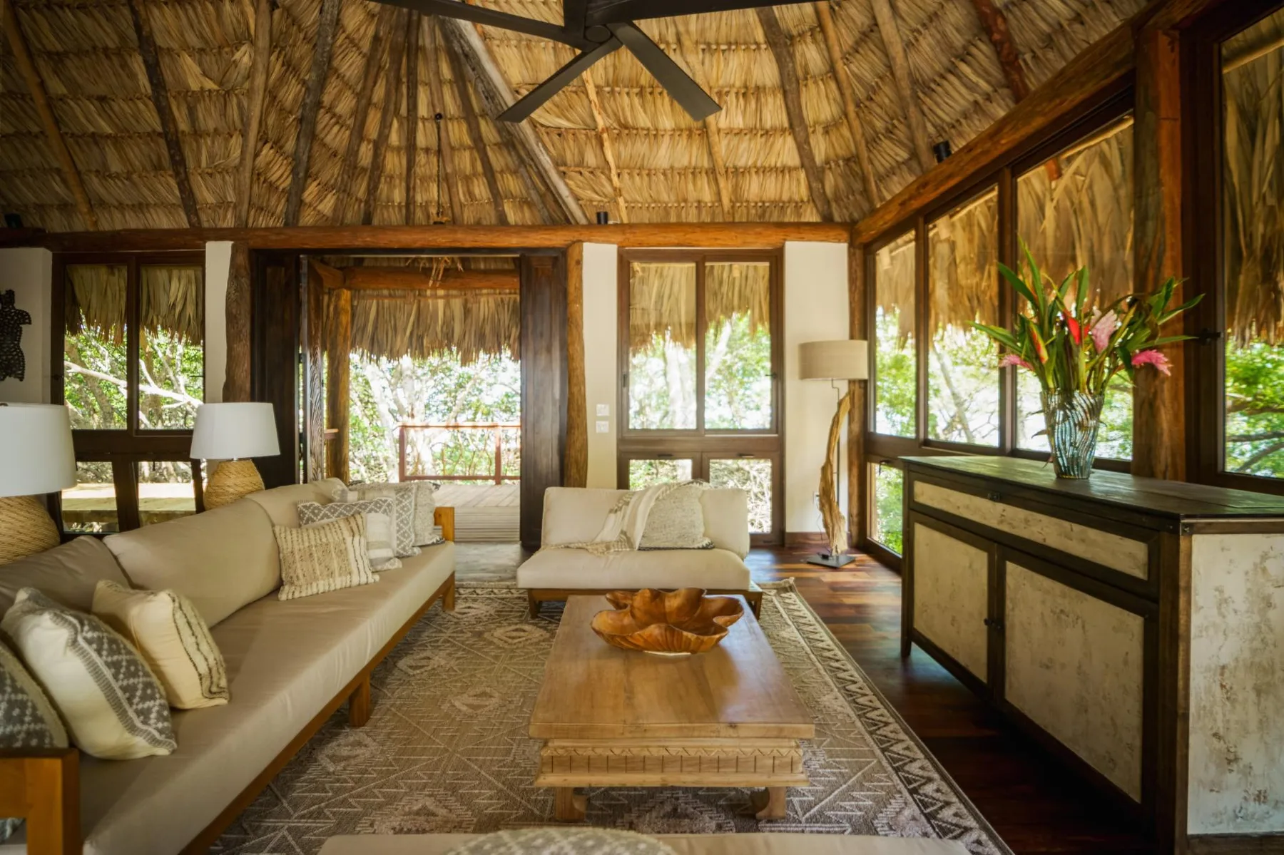 A bright living room has woven seating, a wooden coffee table, and large windows.
