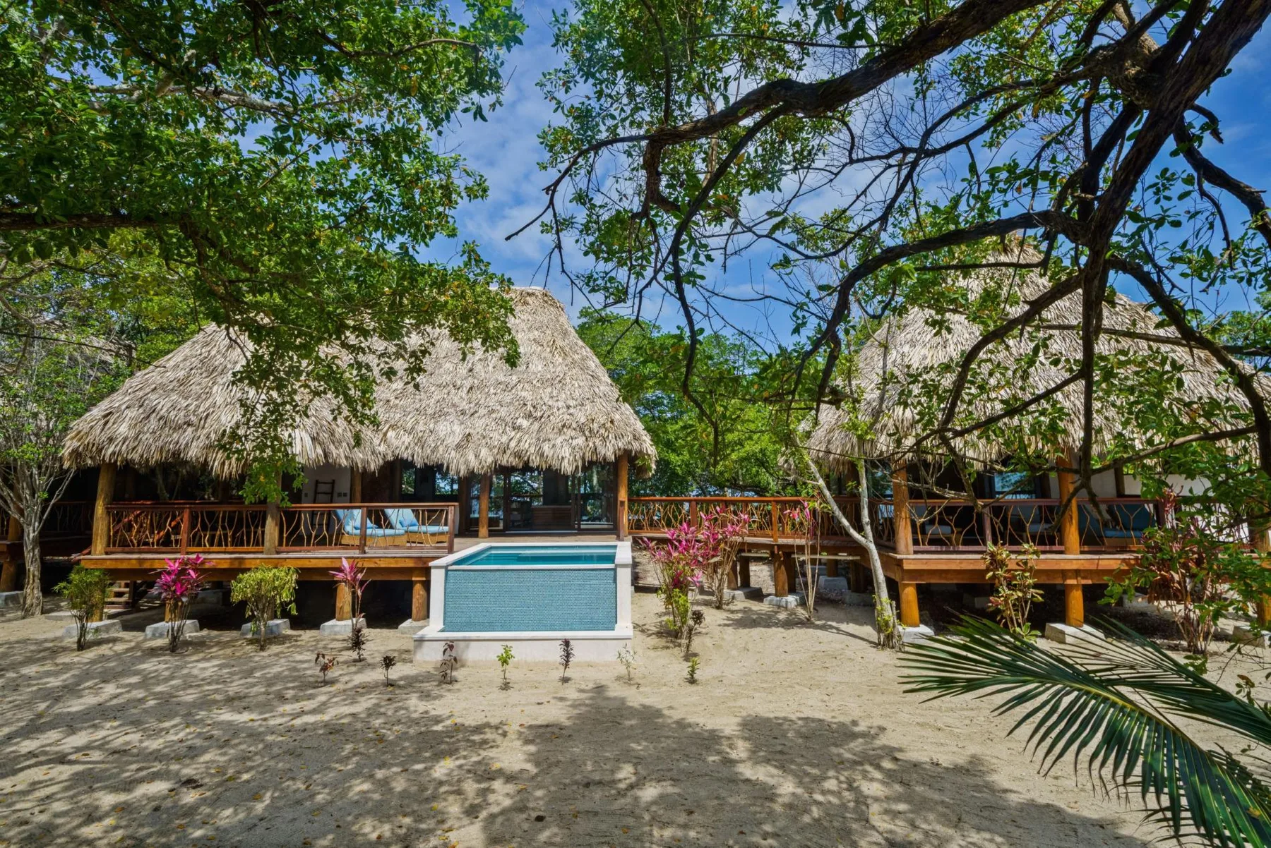 Thatched-roof buildings stand among trees beside a small pool.