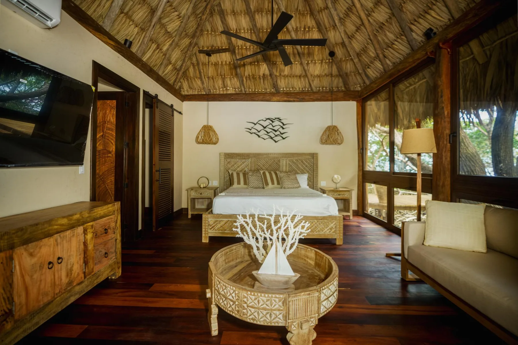 A bedroom with a wooden bed, woven ceiling, and seating area.