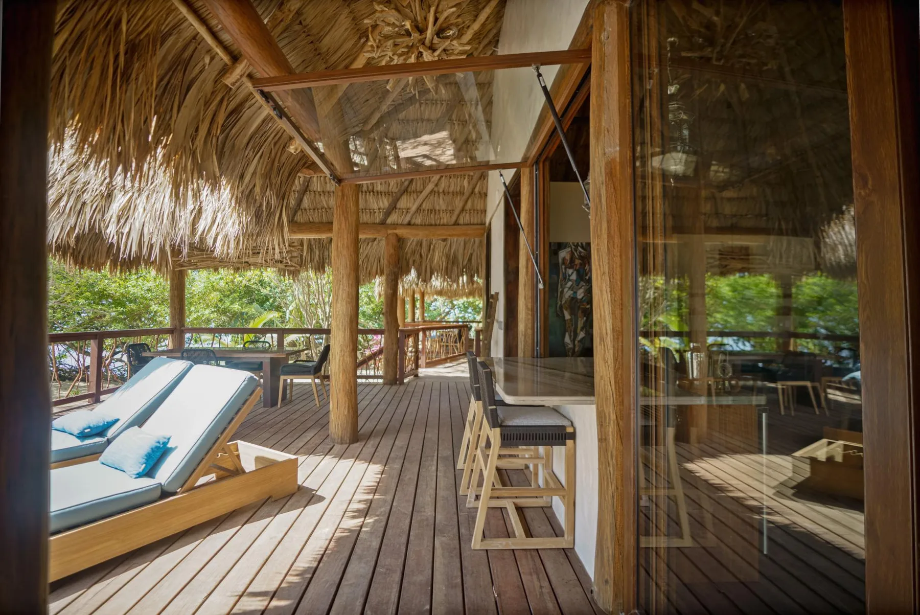 A thatched-roof wooden deck with lounge seating and glass doors.