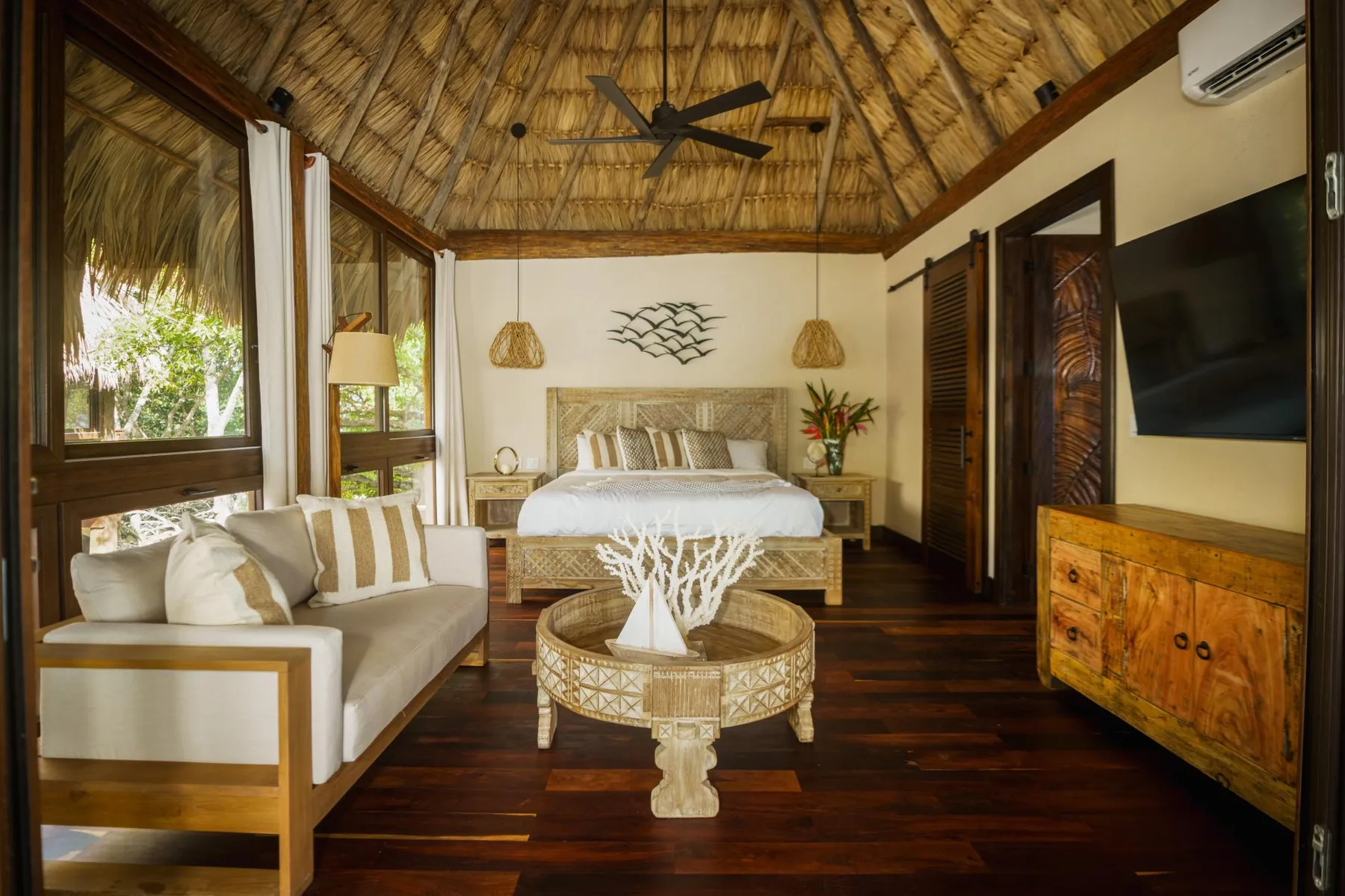 A bedroom with a bed, seating area, and thatched ceiling.