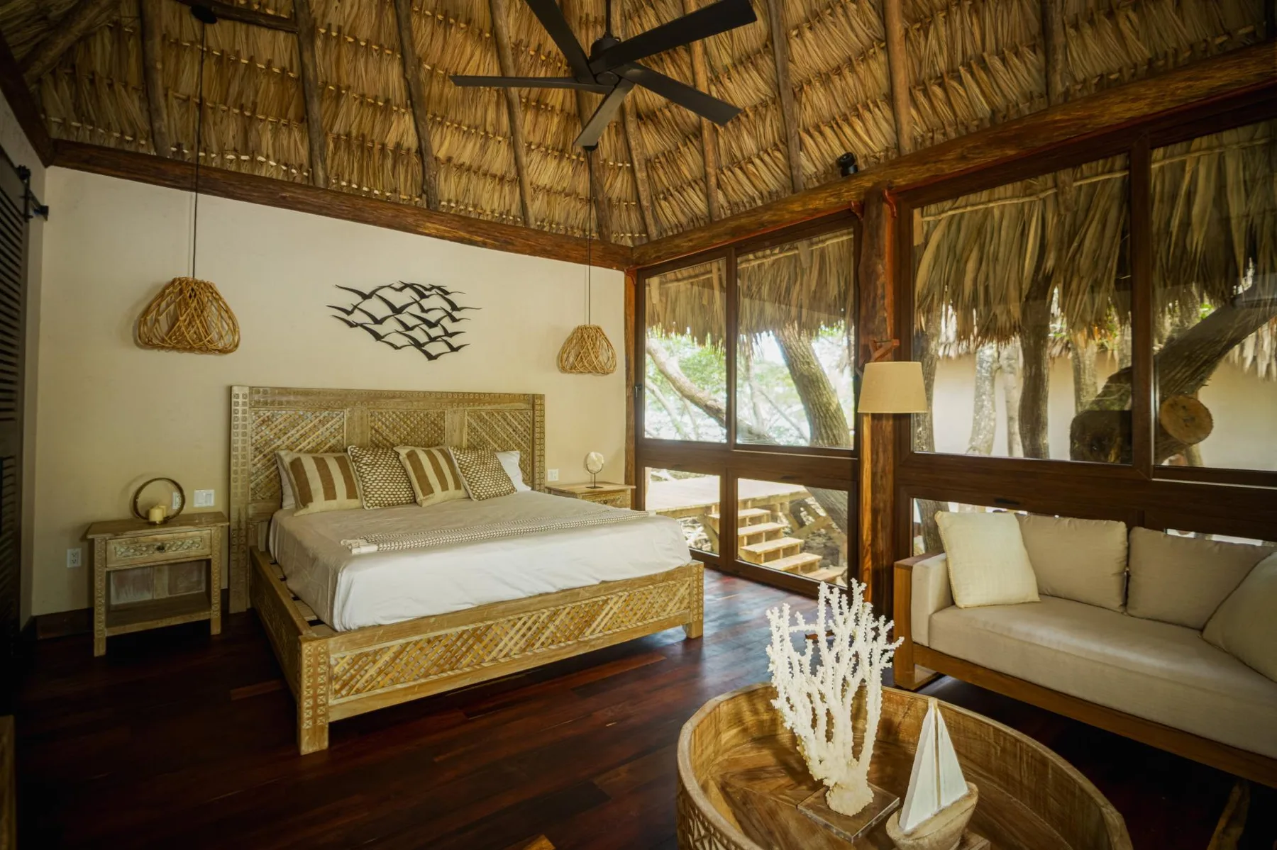 A bedroom with a woven bed, seating area, and thatched ceiling.