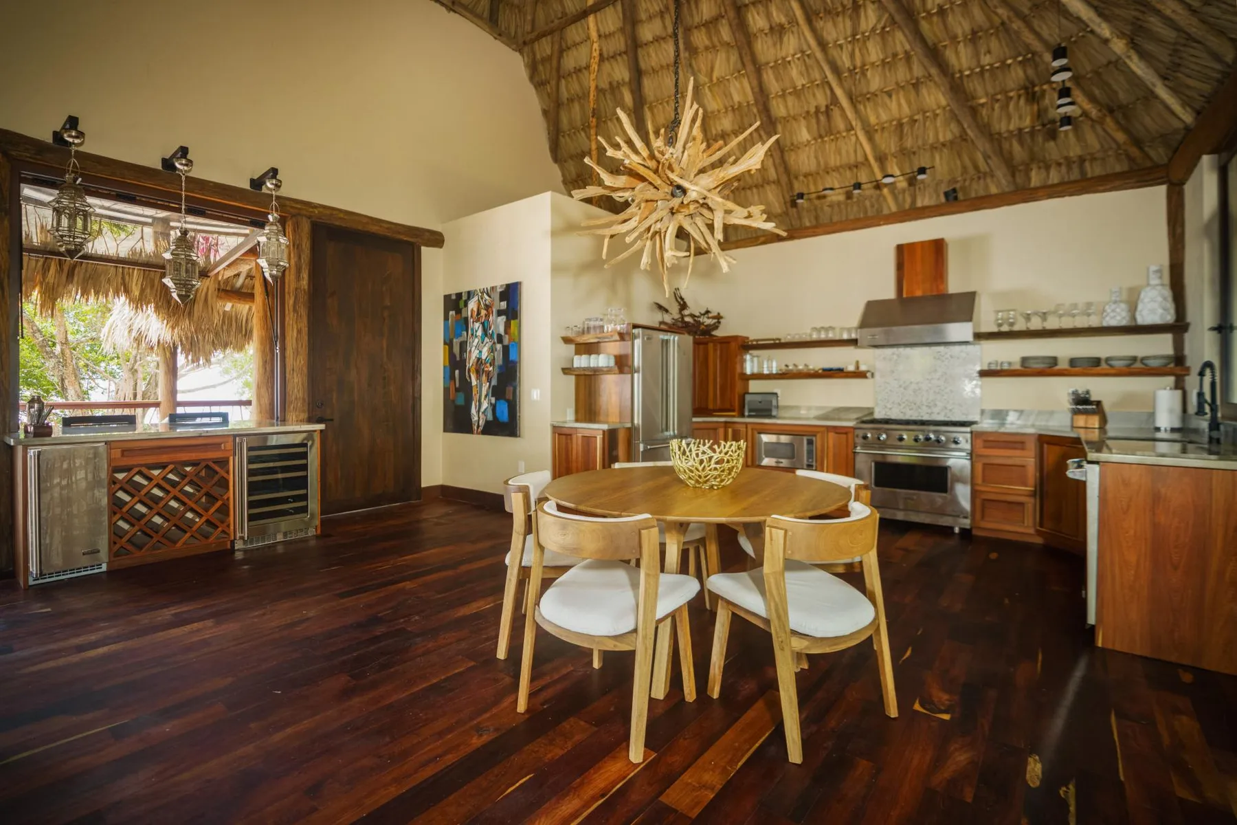 A spacious kitchen and dining area with a round wooden table beneath a thatched ceiling.