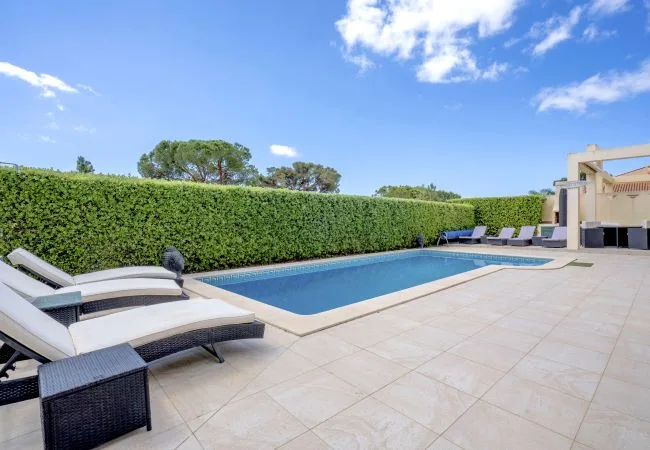 Una piscina al aire libre junto a un patio pavimentado con asientos reclinables.