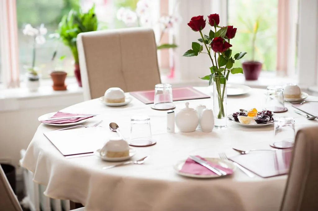 Representative hotel space: A dining table is set with white tableware, pink napkins, and red flowers.