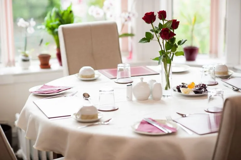 Representative hotel space: A dining table is set with plates, folded napkins, and red roses.