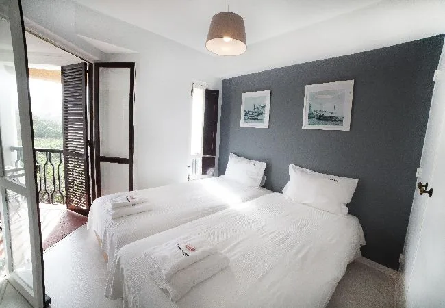 A bright bedroom with two beds and a dark accent wall.