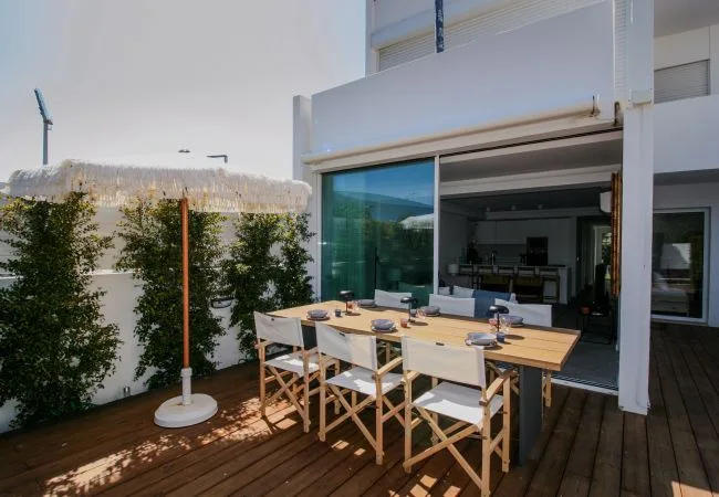 Zona de comedor al aire libre con una mesa larga y asientos sobre una terraza de madera.