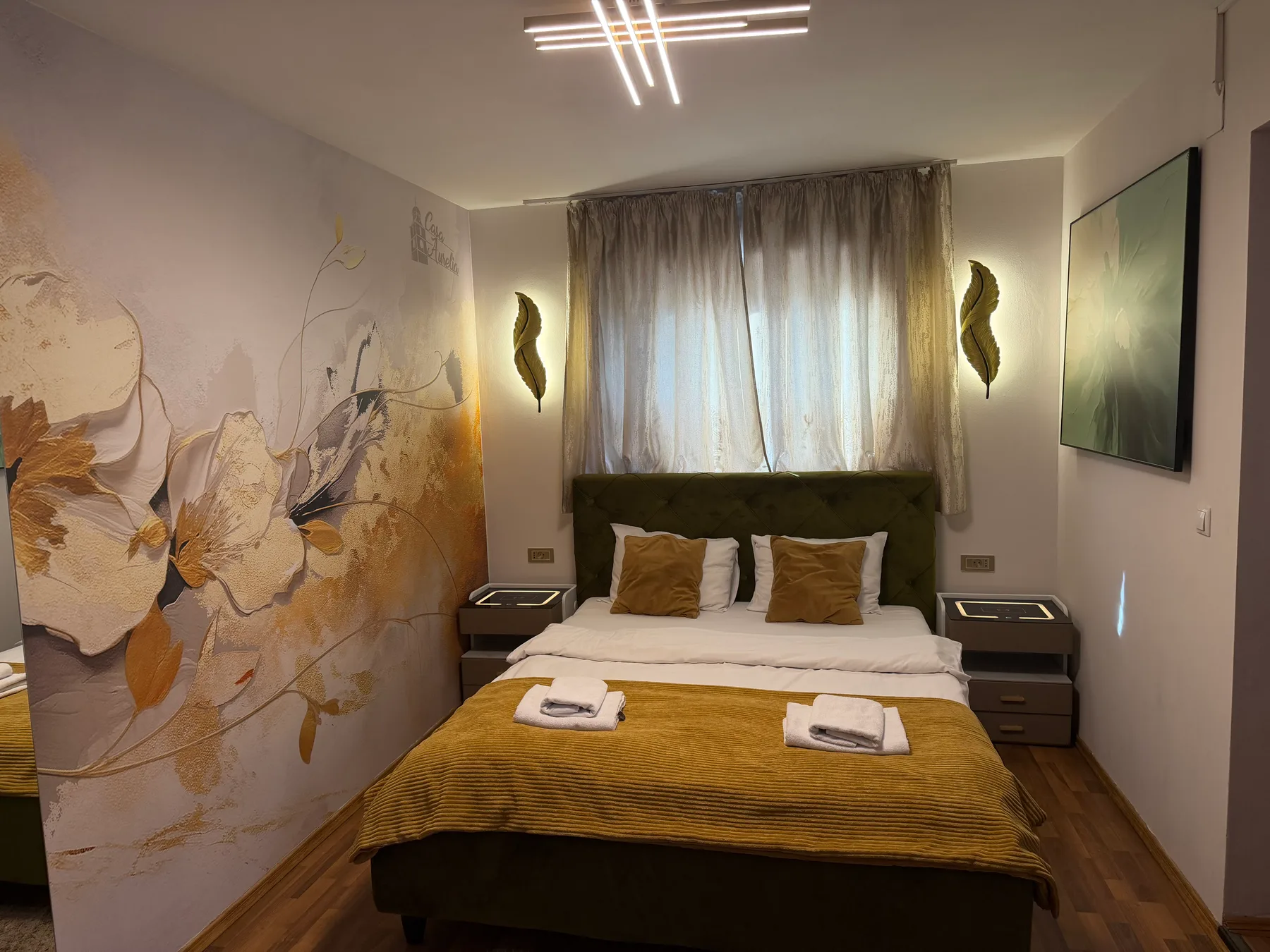 Representative hotel space: A bedroom with a bed, mustard-colored bedding, and floral wall art.