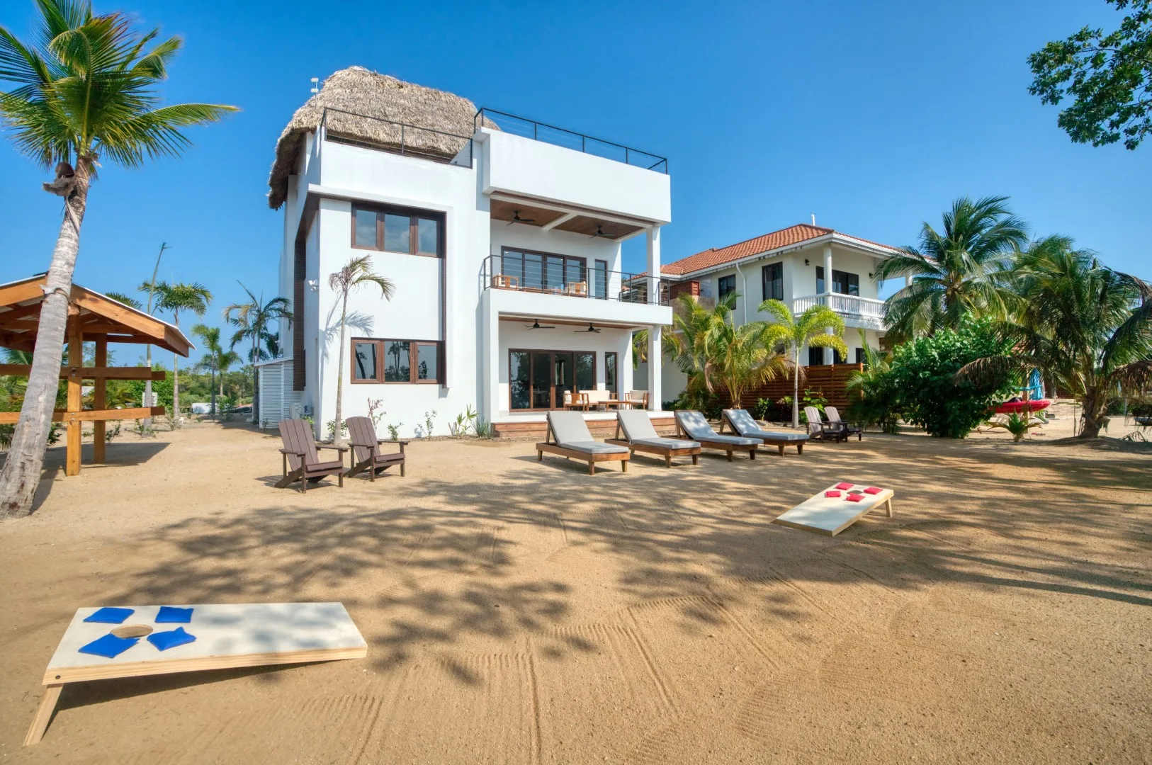 A modern white beachfront building stands beside a sandy outdoor seating area.