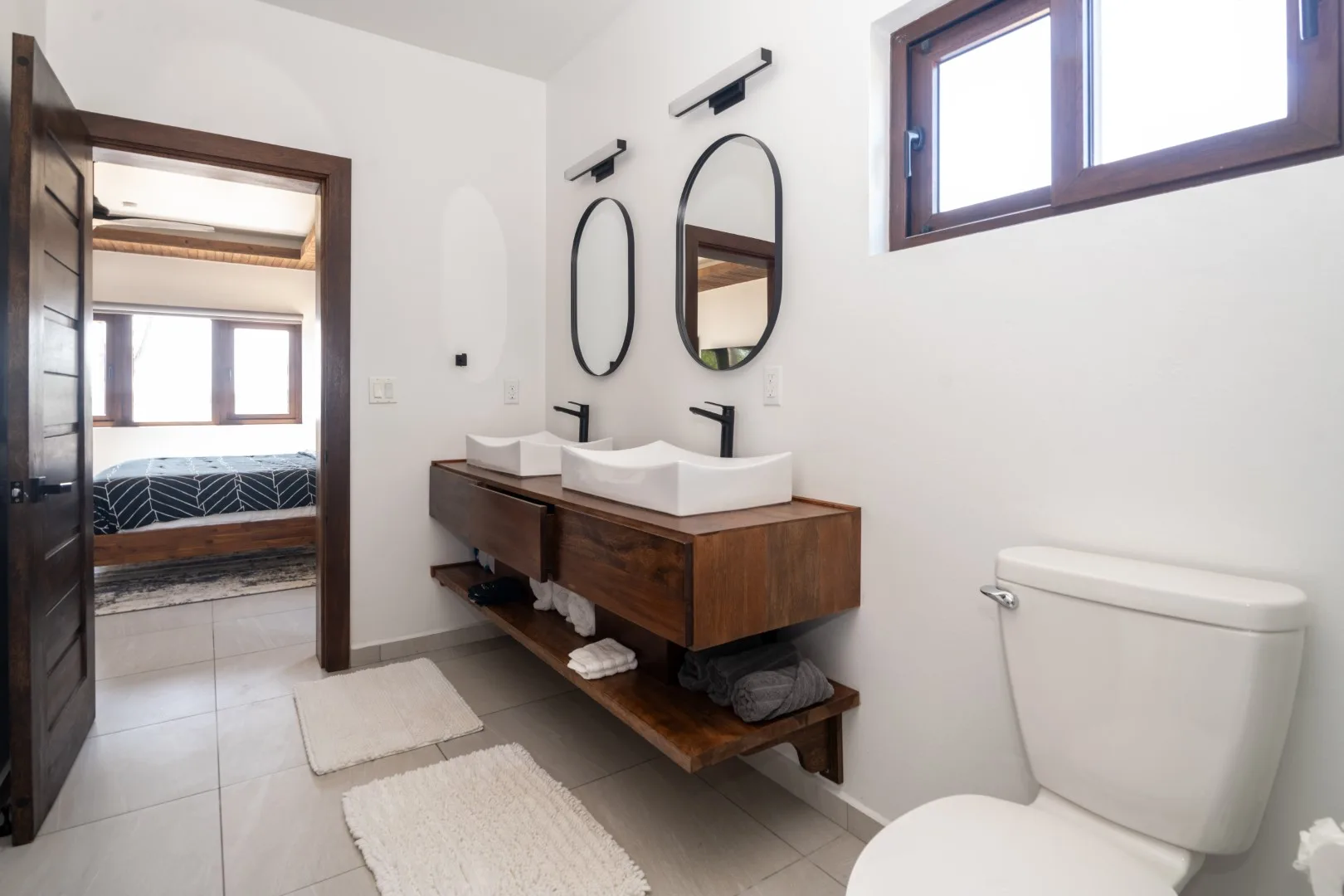 A bright bathroom with a double vanity, mirrors, and a toilet.