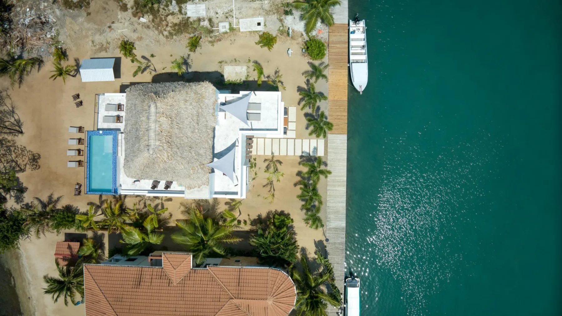 An aerial view shows a waterfront property with a pool and dock beside the water.