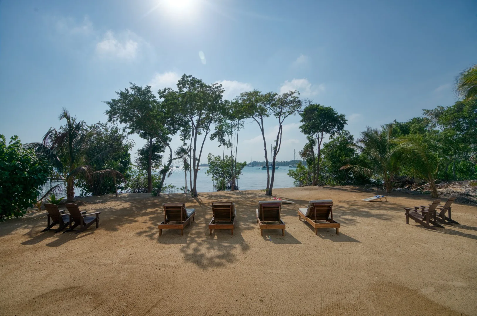 A sandy outdoor seating area faces the water beneath a line of trees.