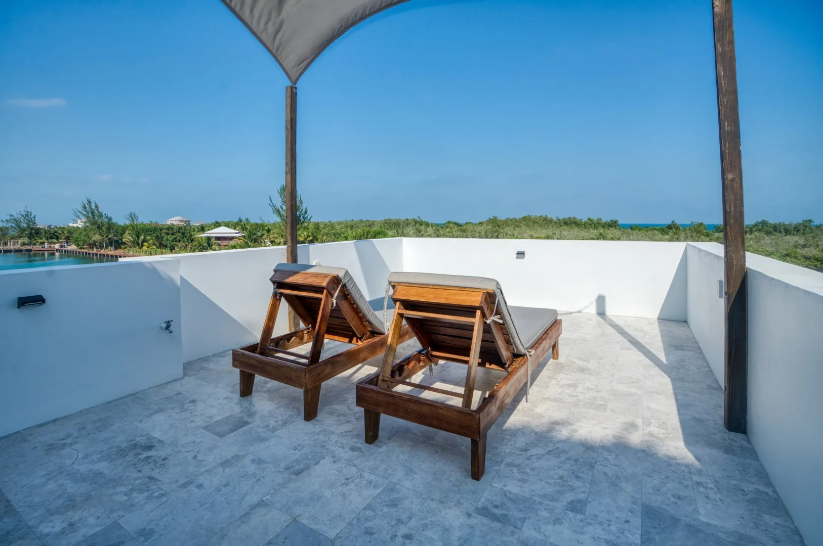 A rooftop terrace has two wooden loungers beneath a shade canopy.