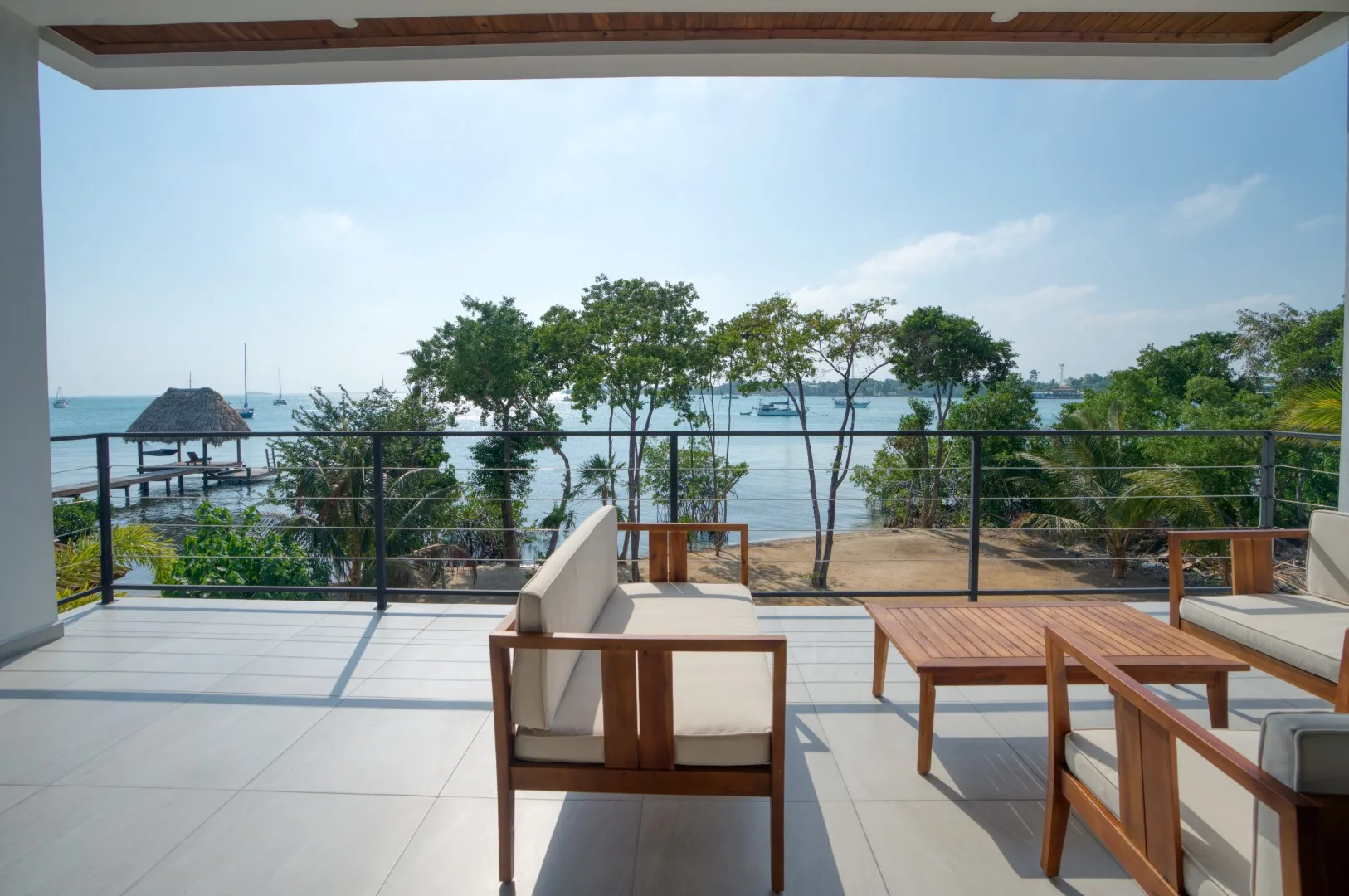 A covered outdoor terrace with seating and a view of trees and water.