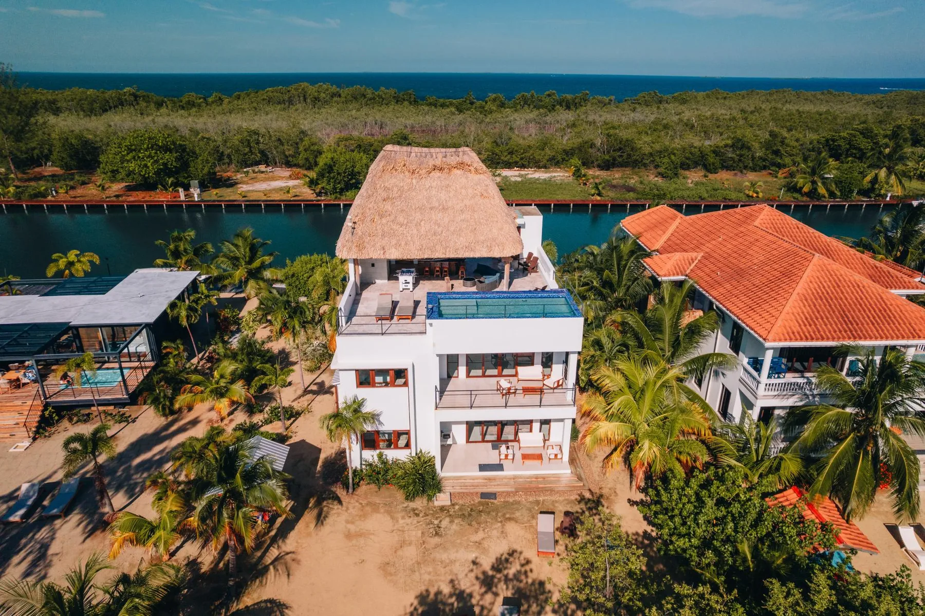 Aerial view of a coastal resort with red-roofed buildings, palms, and the sea.