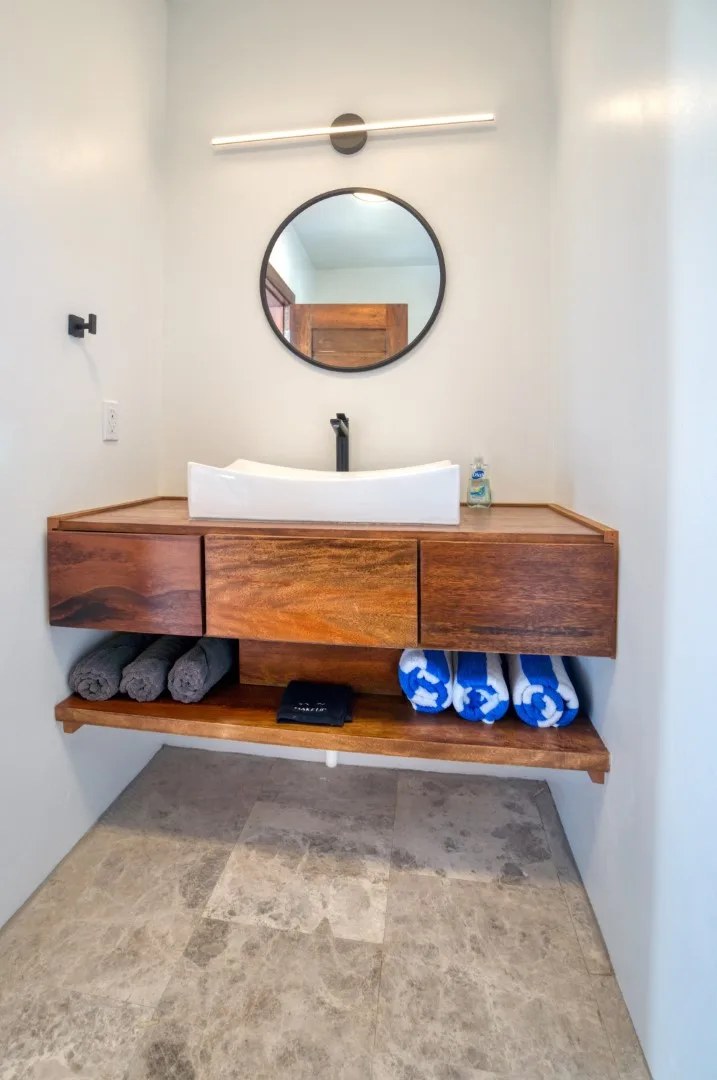 A bathroom vanity with a vessel sink and round mirror above the wooden cabinet.