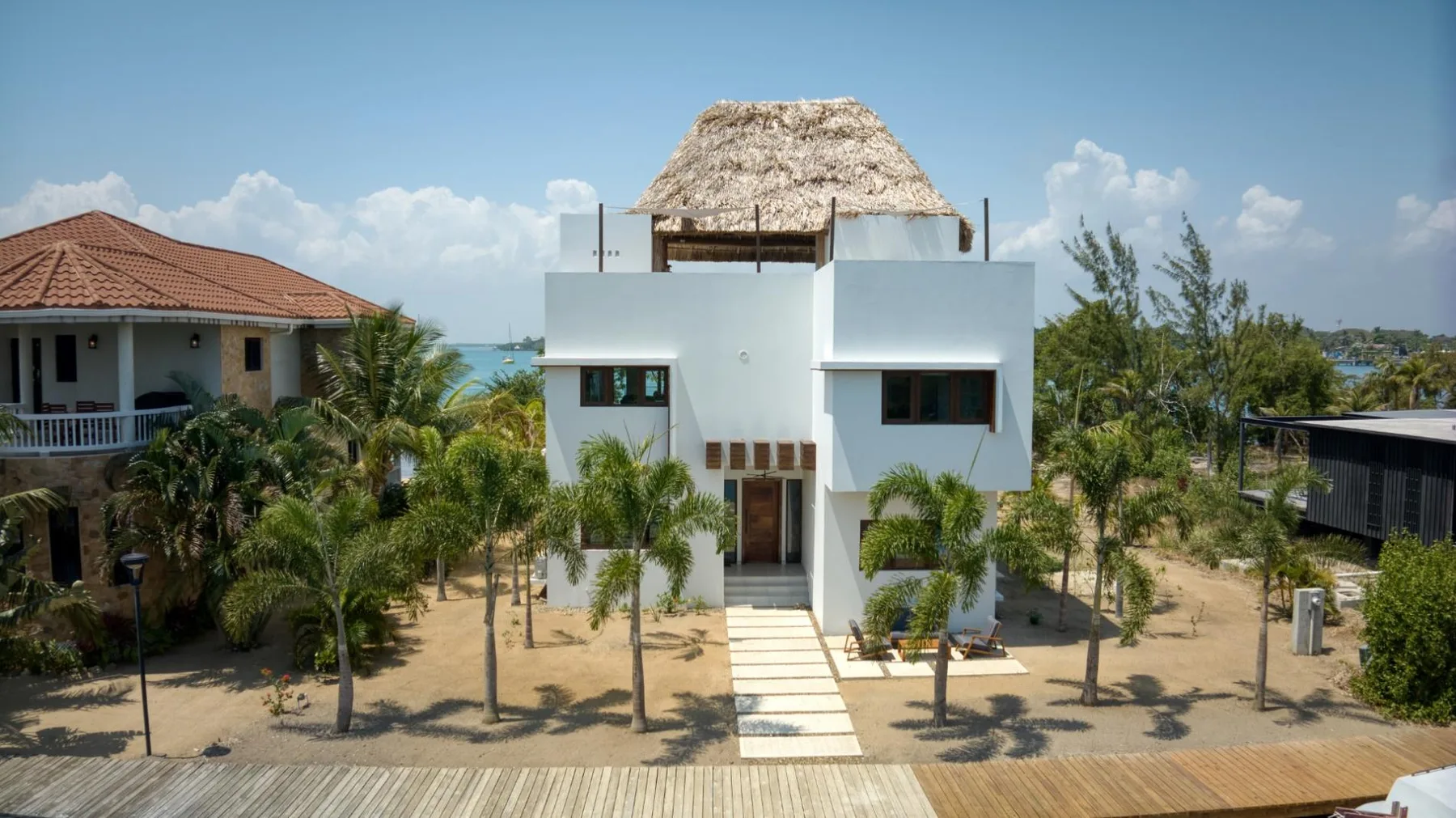A modern white building stands among palm trees beside a wooden boardwalk.