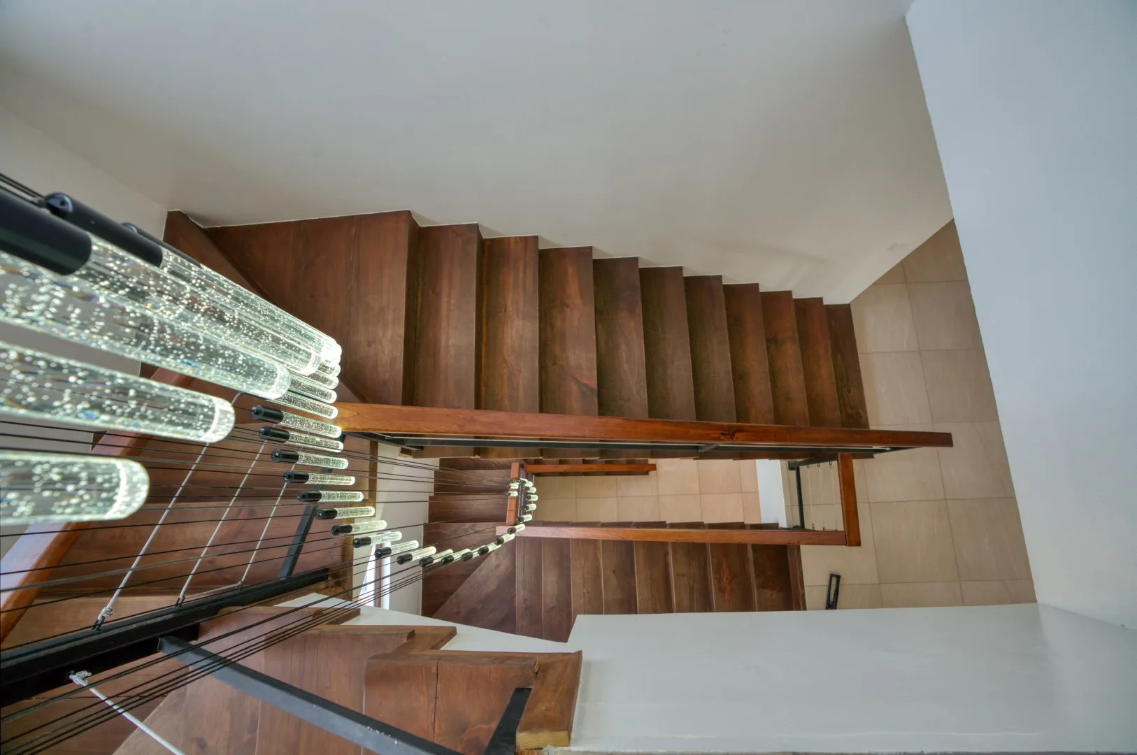A wooden staircase with a metal railing runs beside a tiled wall.