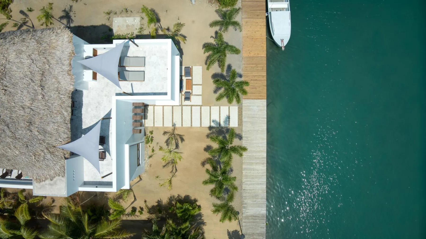 An aerial view shows a beachfront building beside a wooden pier and turquoise water.