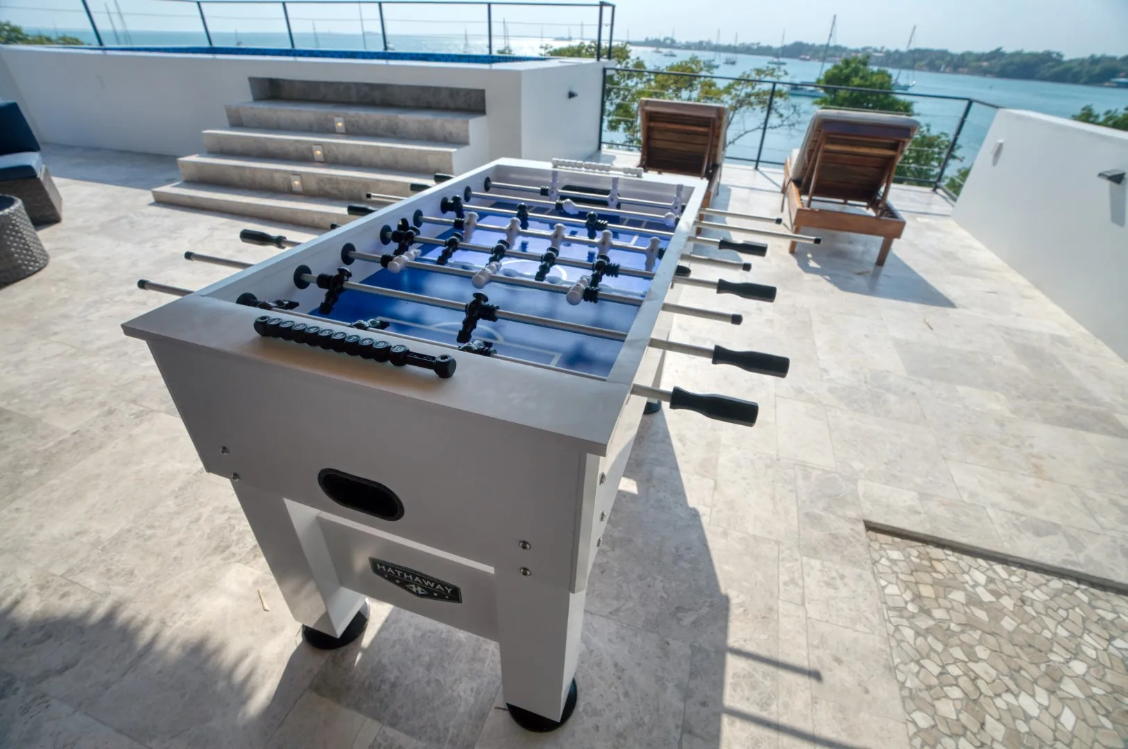 A foosball table sits on a rooftop terrace overlooking the water.