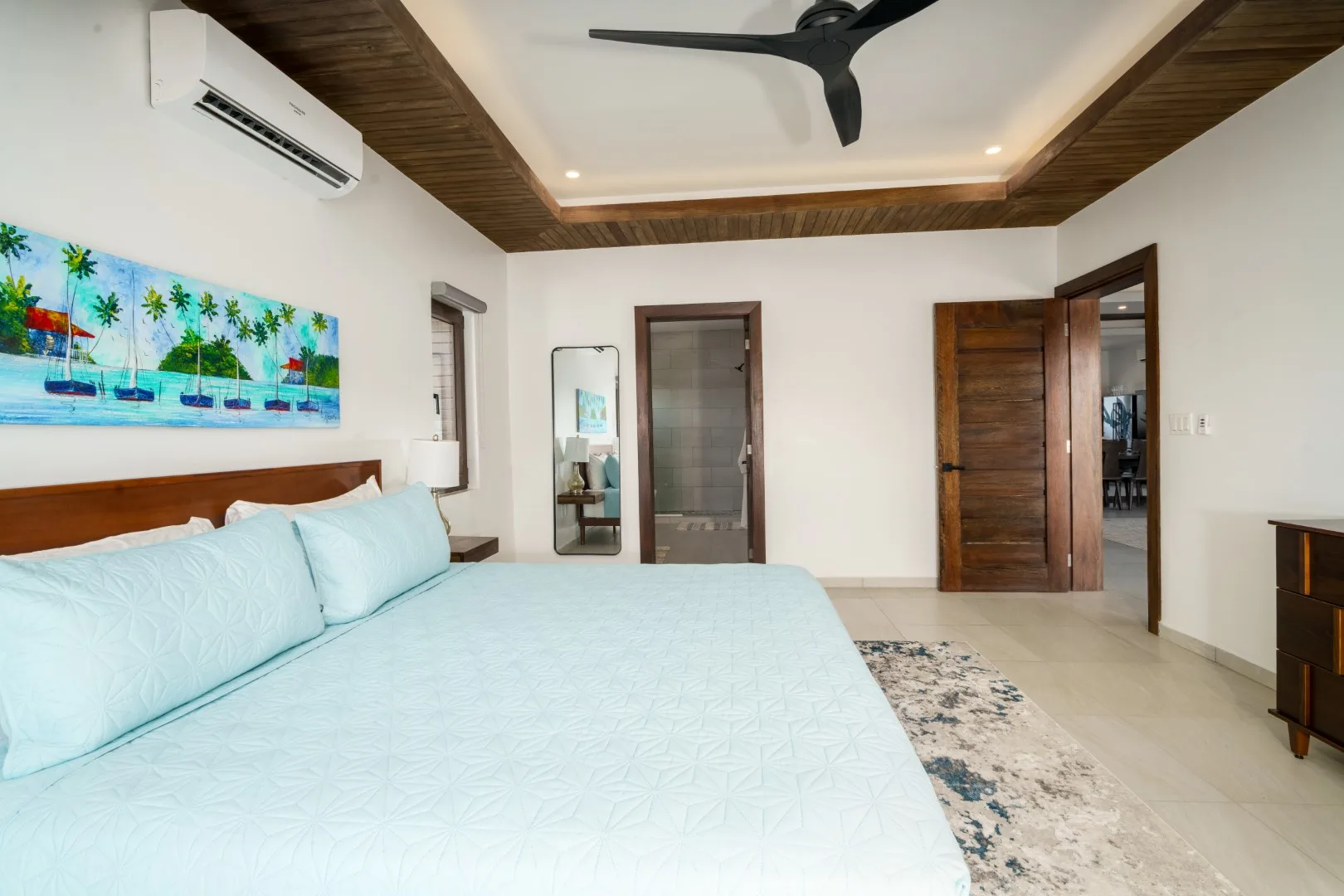 A bedroom with a large bed, tropical wall art, and a ceiling fan.