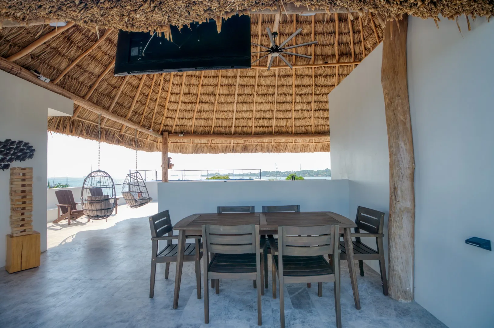 A covered outdoor dining area with a table and chairs beneath a thatched roof.