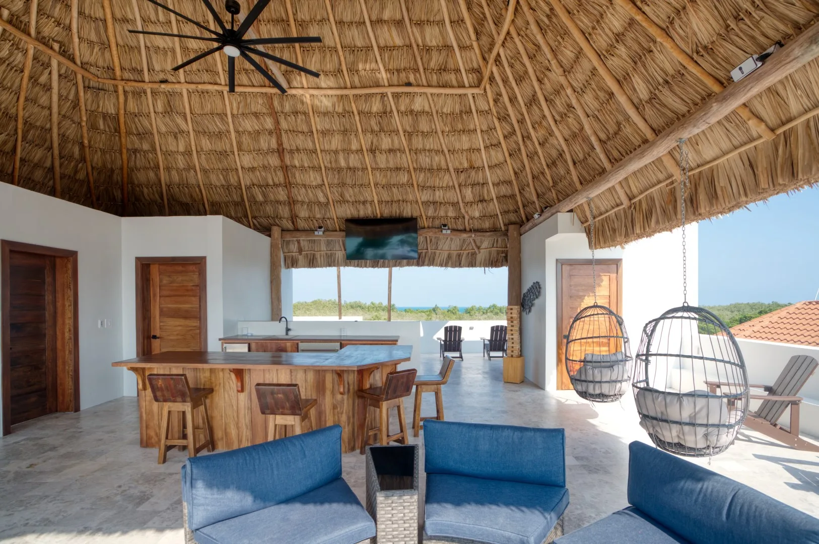 An open-air lounge with a wooden bar, blue seating, and a thatched roof.
