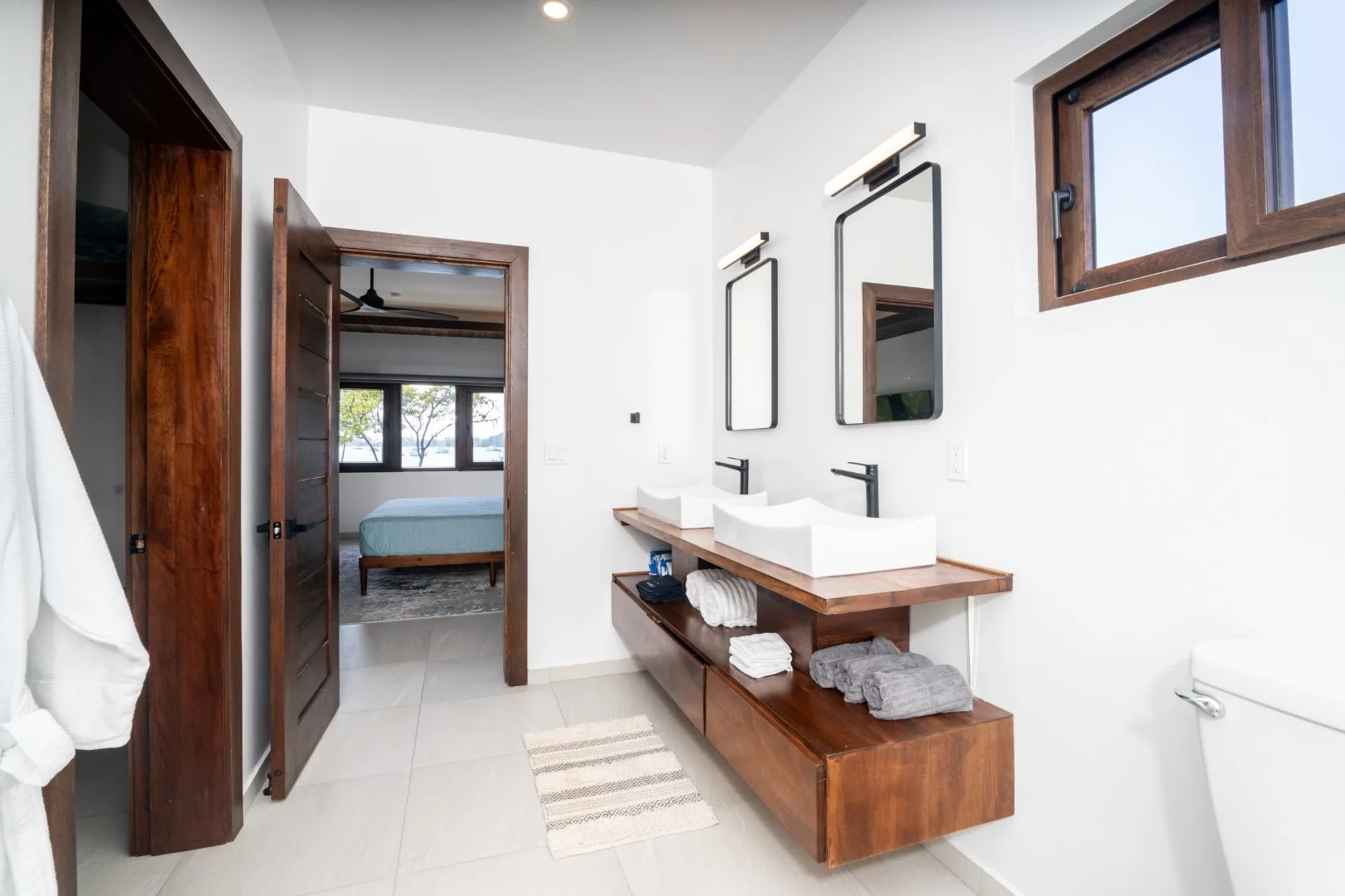 A bright bathroom has a double vanity with mirrors and an open doorway.