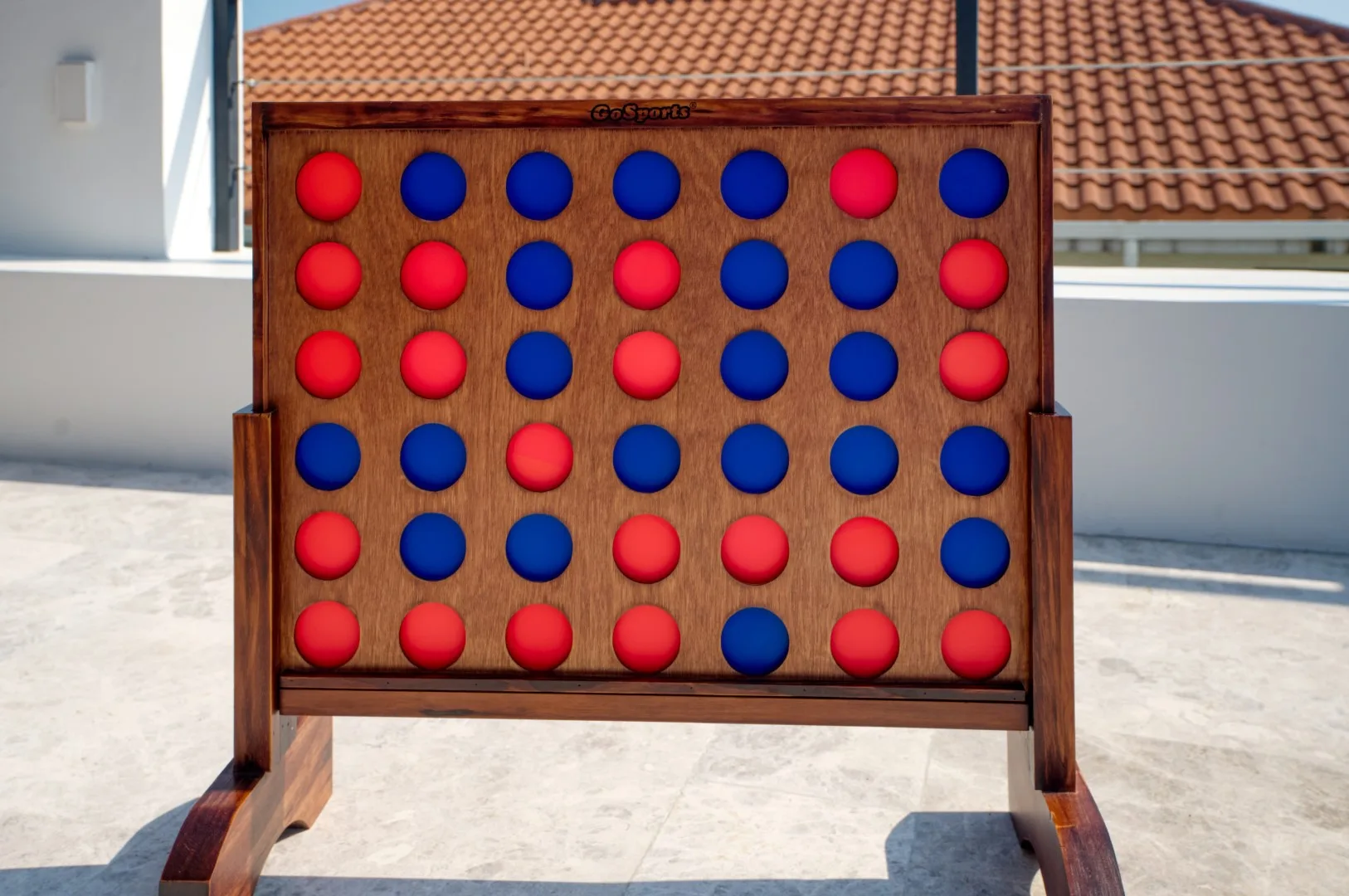 A large wooden connect-four game stands on a sunlit outdoor patio.