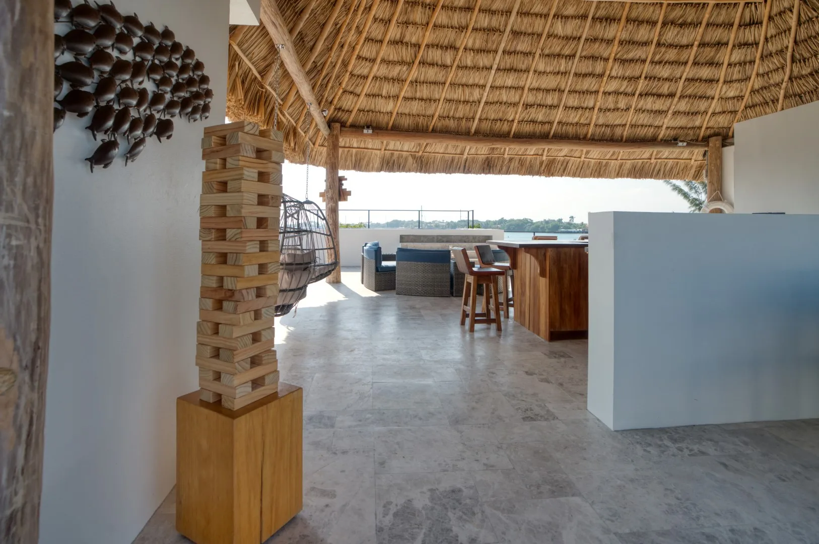 An open-air bar and seating area beneath a thatched roof, with a counter facing the water.