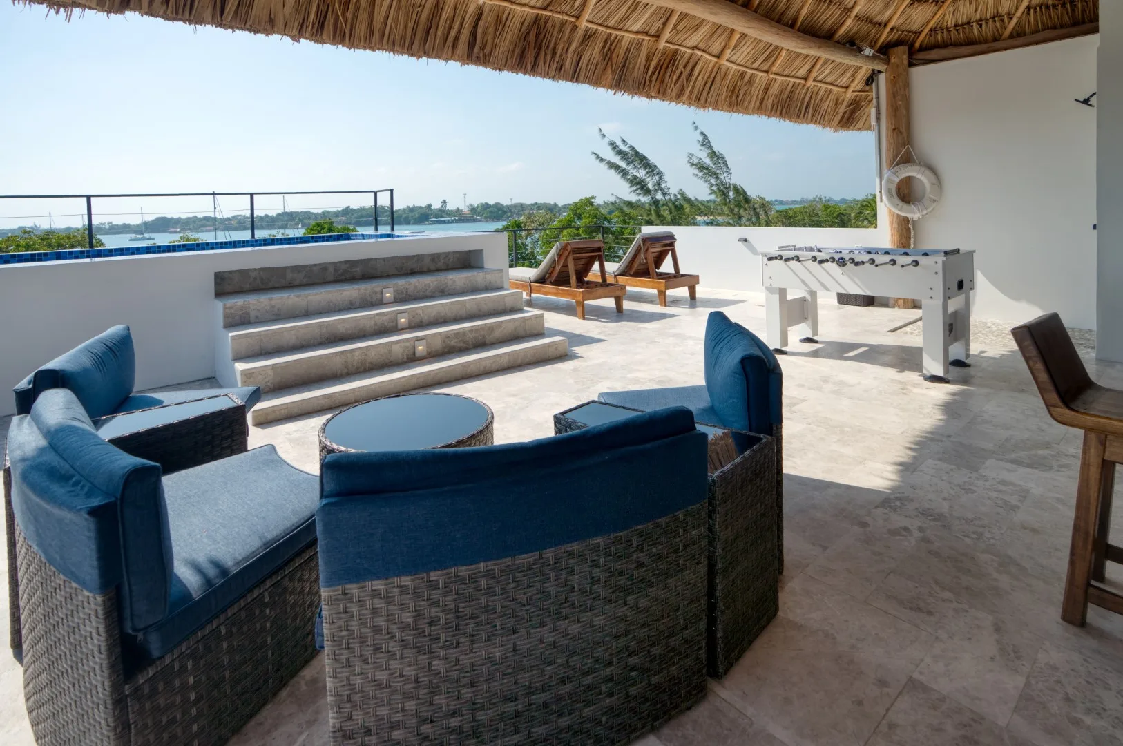 A shaded rooftop terrace has lounge seating, a table, and a foosball table.