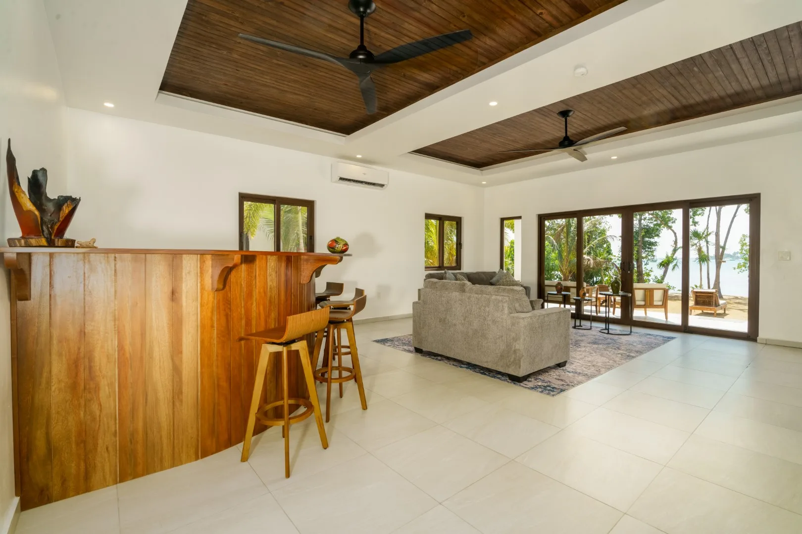 A bright open-plan living room with a wooden bar and seating beside large glass doors.