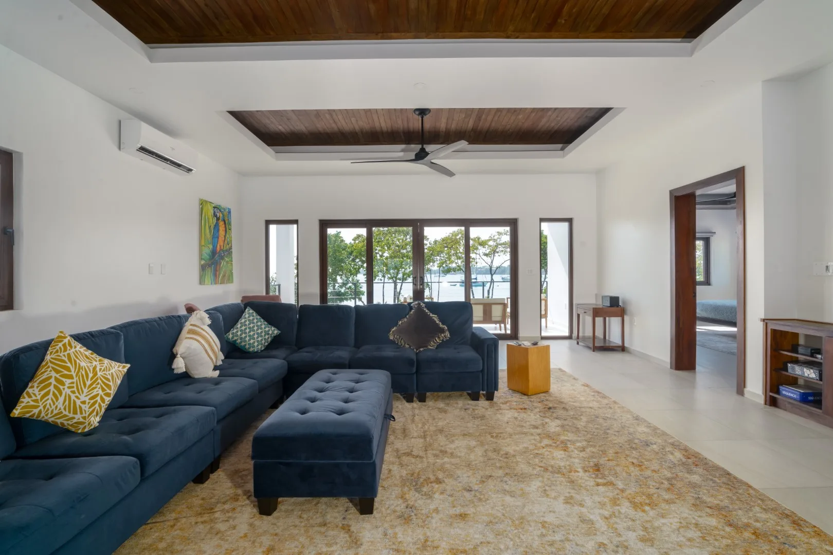 A bright living room with dark seating, a matching ottoman, and wide glass doors.