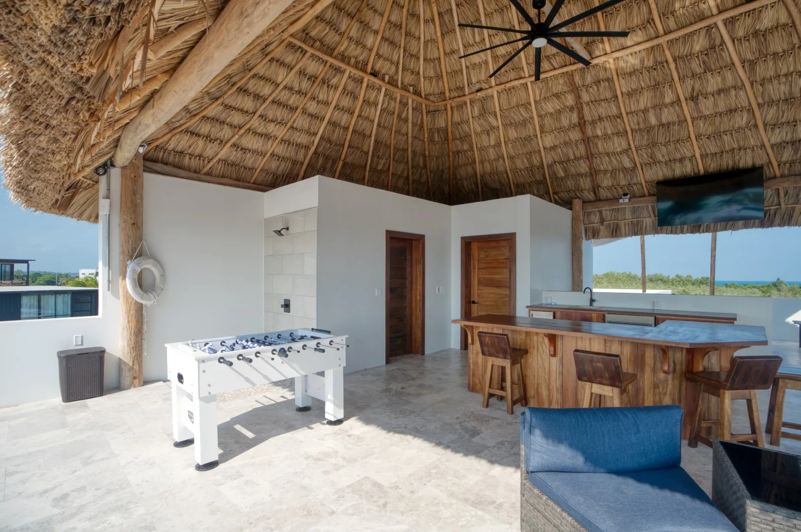 An open-air entertainment area with a foosball table, bar seating, and a thatched roof.
