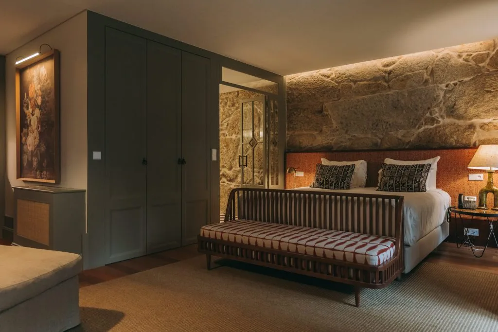 Espacio representativo del hotel: Dormitorio con una cama, un banco de madera y armarios empotrados oscuros.