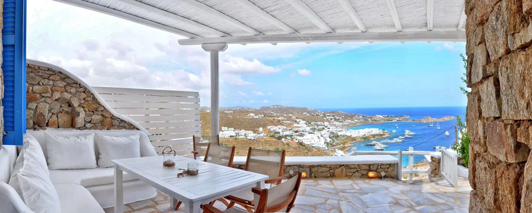 A covered outdoor dining area with seating overlooks a coastal bay.