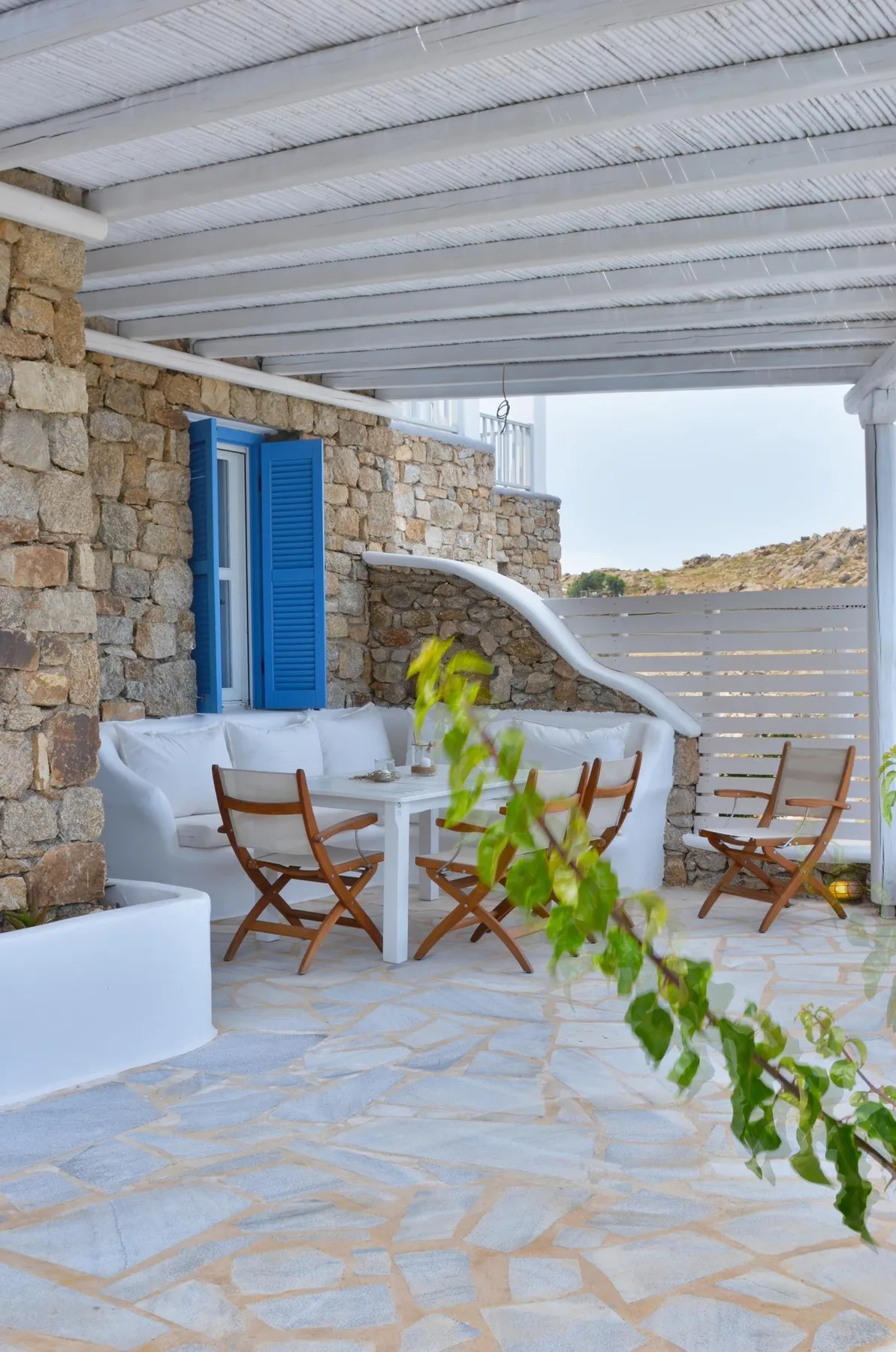 A covered stone patio with outdoor seating and bright blue shutters.