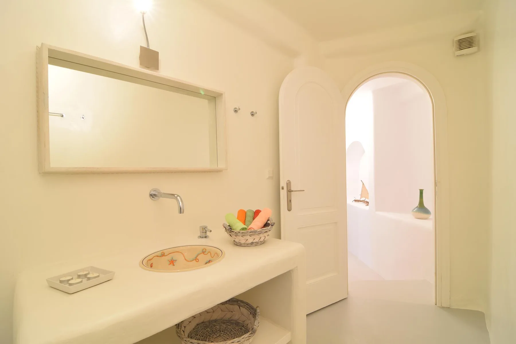 A bathroom vanity with a wall mirror and an open arched doorway.