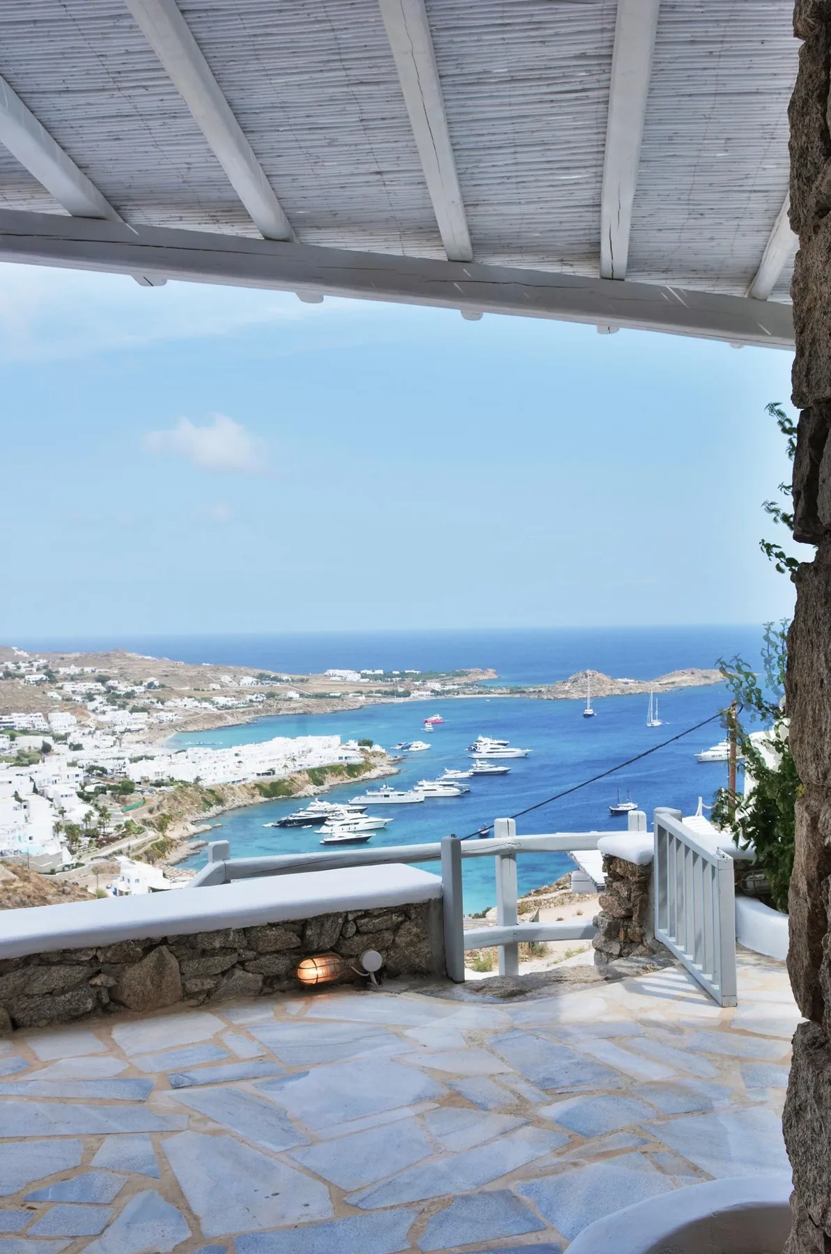 A stone terrace overlooks a coastal bay with boats and a distant shoreline.