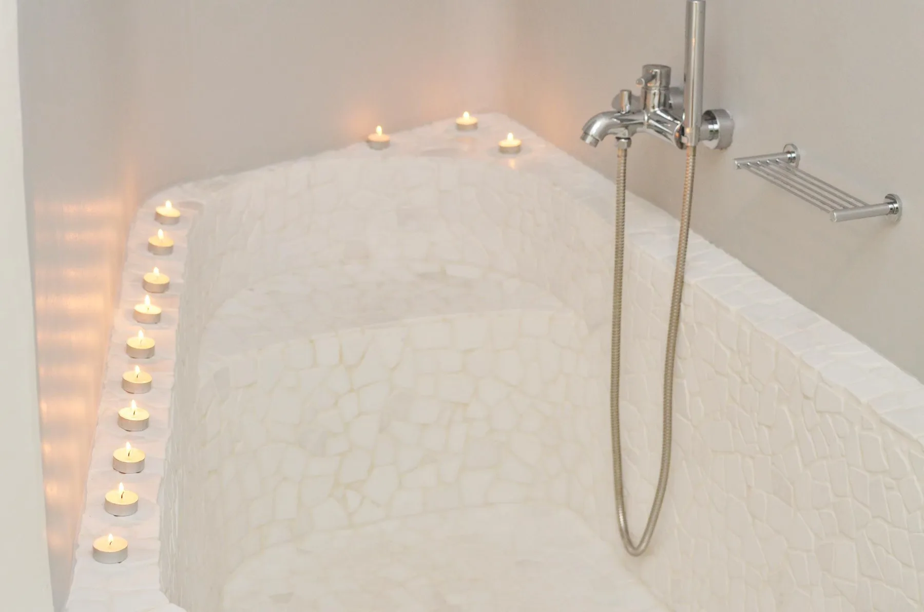 A curved tiled shower area has small candles arranged along its edge.