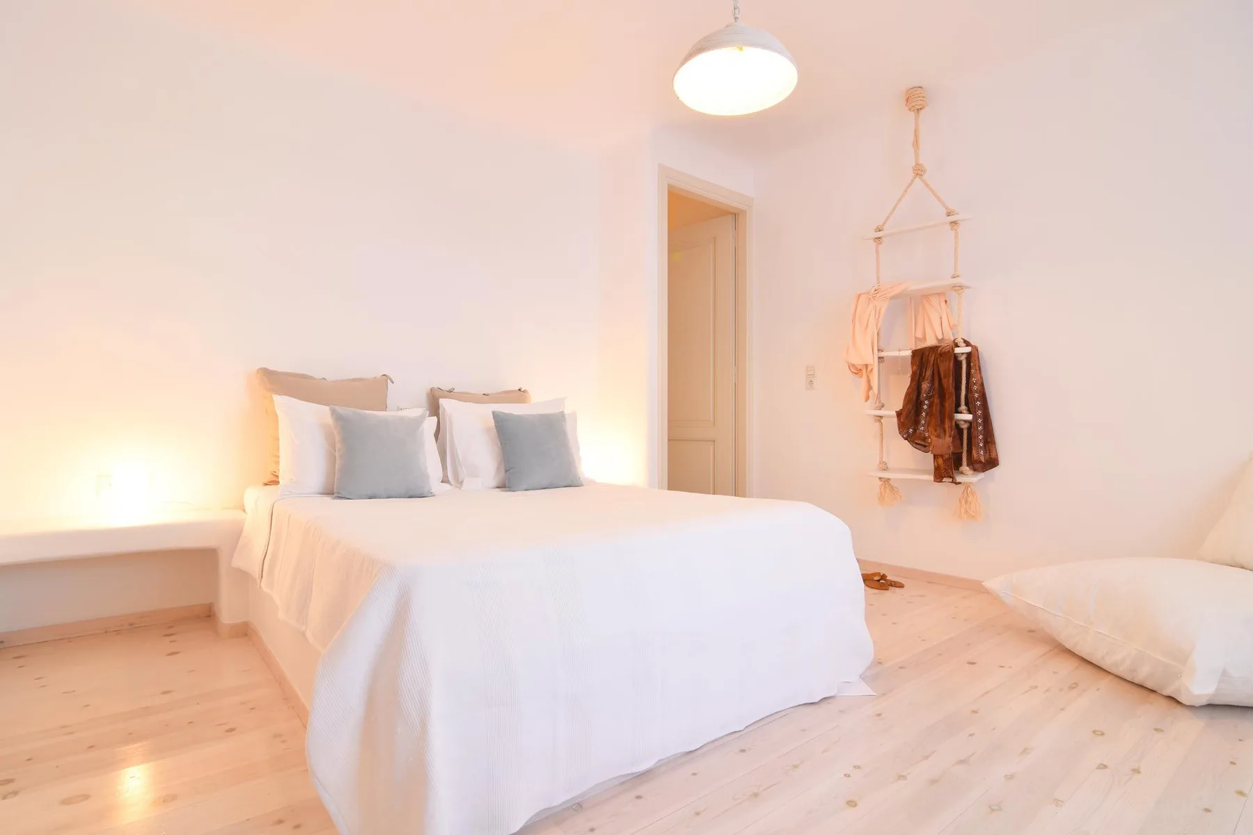 A bright bedroom with a white bed and clothes hanging on the wall.